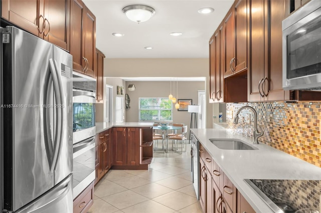 kitchen featuring appliances with stainless steel finishes, backsplash, sink, light tile patterned floors, and decorative light fixtures