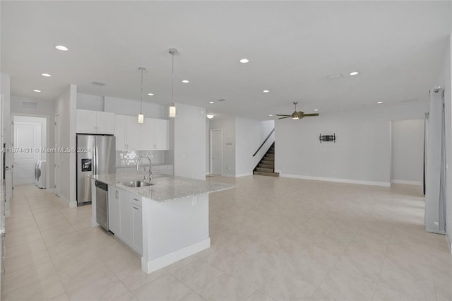 kitchen with a center island with sink, sink, decorative light fixtures, white cabinetry, and light stone counters