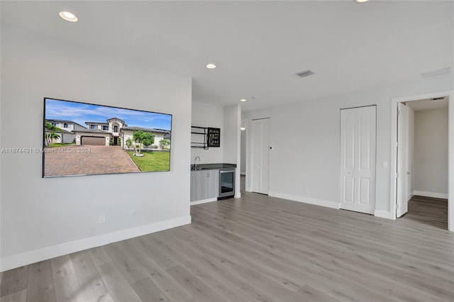 unfurnished living room featuring wine cooler, sink, and hardwood / wood-style flooring