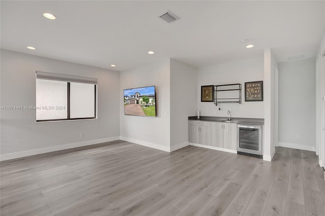 bar featuring light hardwood / wood-style flooring, sink, and beverage cooler