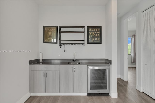 bar featuring sink, beverage cooler, and light wood-type flooring