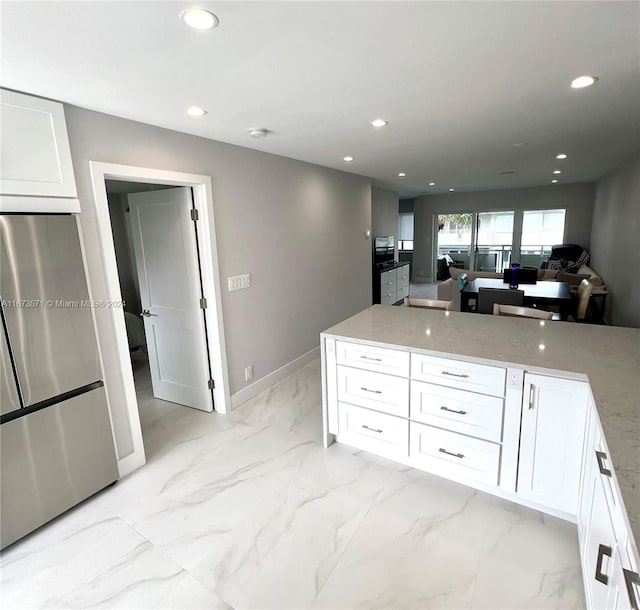 kitchen with light stone counters, stainless steel fridge, and white cabinetry