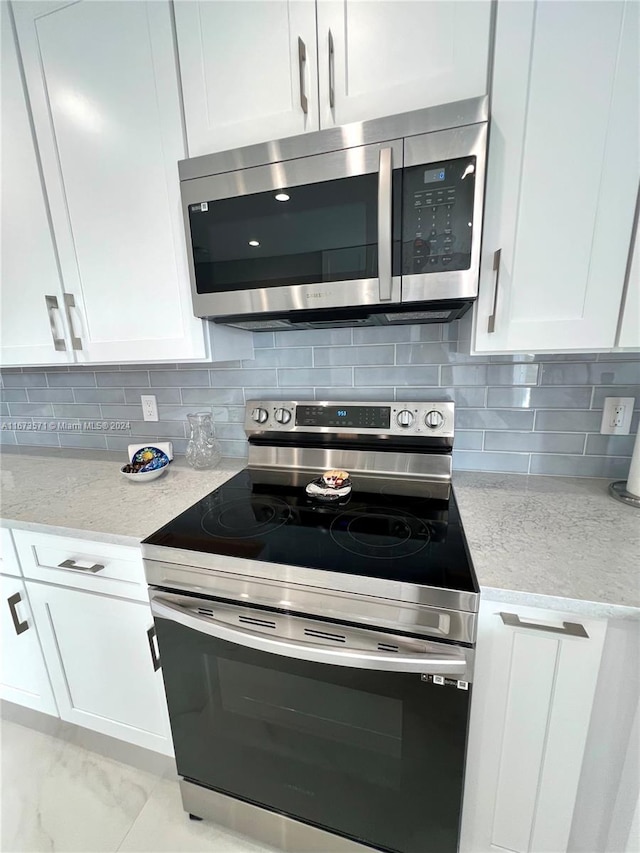 kitchen with appliances with stainless steel finishes, light stone counters, tasteful backsplash, and white cabinets