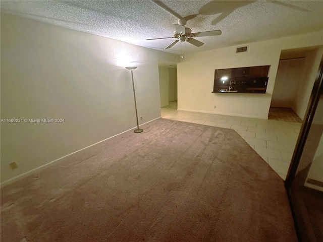 carpeted empty room with ceiling fan, sink, and a textured ceiling