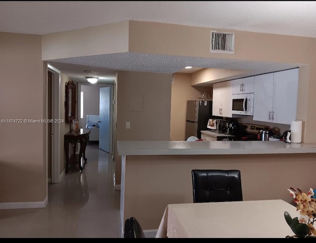 kitchen with light tile patterned flooring, kitchen peninsula, white cabinets, appliances with stainless steel finishes, and a textured ceiling