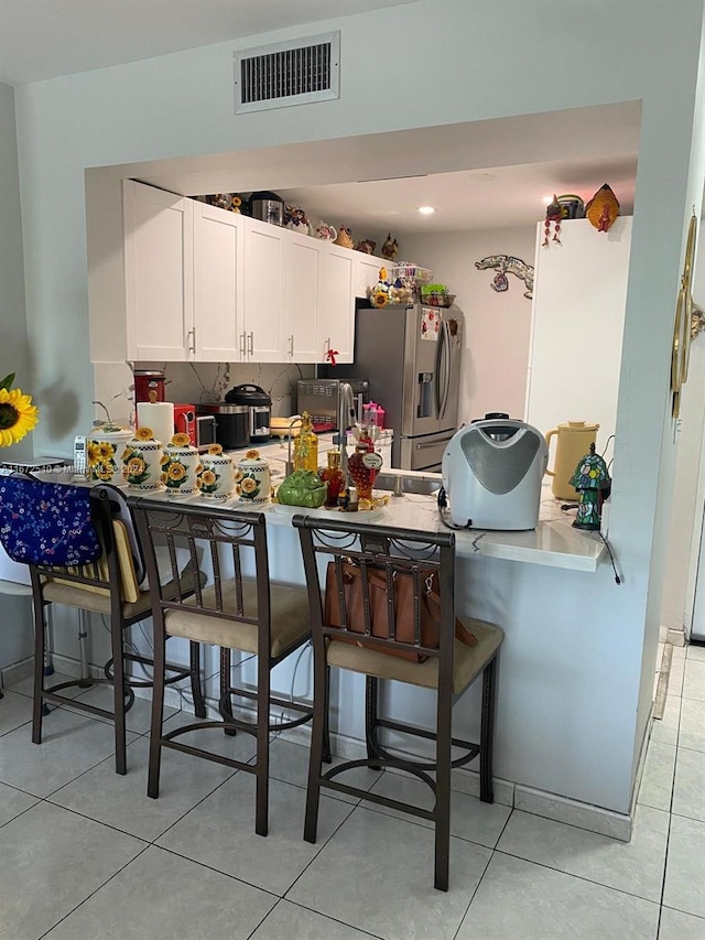 kitchen featuring stainless steel fridge, a breakfast bar, kitchen peninsula, and white cabinetry