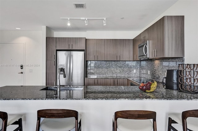 kitchen with tasteful backsplash, dark stone countertops, sink, kitchen peninsula, and appliances with stainless steel finishes