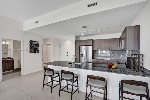 kitchen with kitchen peninsula, sink, dark brown cabinets, stainless steel fridge with ice dispenser, and dark stone counters