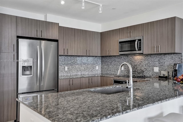 kitchen featuring decorative backsplash, dark stone countertops, sink, kitchen peninsula, and appliances with stainless steel finishes