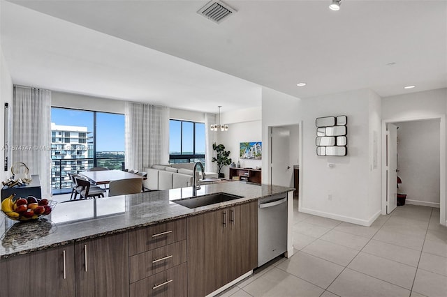 kitchen featuring an inviting chandelier, dark stone countertops, sink, stainless steel dishwasher, and light tile patterned floors