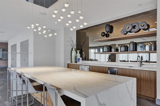 interior space featuring stainless steel refrigerator, a kitchen breakfast bar, sink, light stone counters, and hanging light fixtures