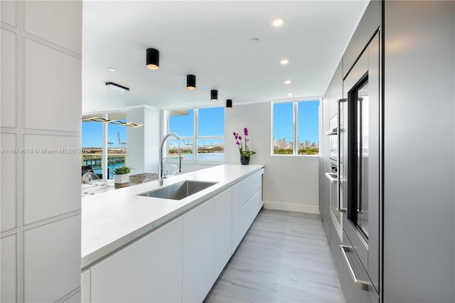 kitchen featuring a water view, light hardwood / wood-style floors, decorative light fixtures, sink, and white cabinetry