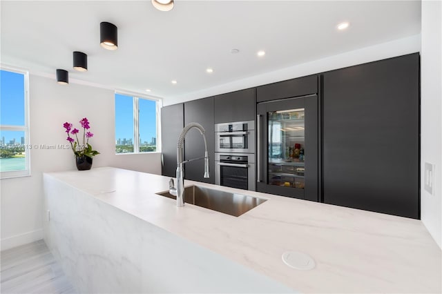 kitchen featuring light stone counters, sink, kitchen peninsula, double oven, and light wood-type flooring