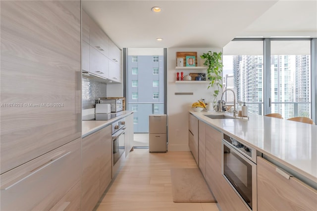 kitchen featuring sink, light hardwood / wood-style flooring, black electric cooktop, stainless steel oven, and decorative backsplash