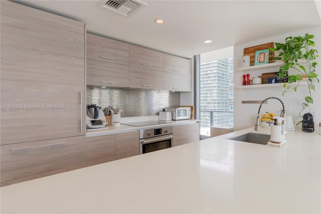 kitchen featuring light brown cabinetry, oven, sink, backsplash, and black electric stovetop