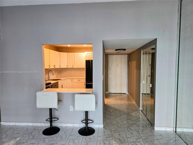 kitchen with sink, white cabinetry, a kitchen bar, tasteful backsplash, and black fridge