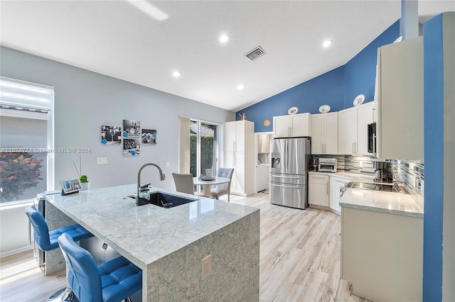 11088 Indian Lake Cir, Boynton Beach, FL 33437 - kitchen with stainless steel fridge, light wood-style flooring, light stone countertops, a center island with sink, and backsplash
