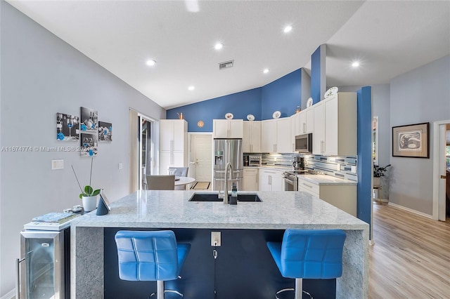 kitchen featuring an island with sink, lofted ceiling, stainless steel appliances, sink, and light hardwood / wood-style flooring