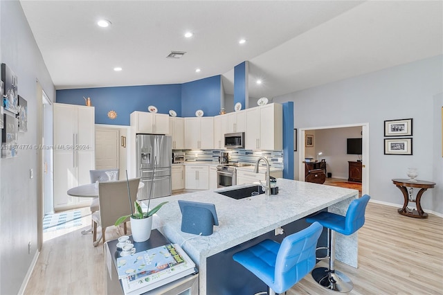 kitchen with a kitchen bar, appliances with stainless steel finishes, sink, and high vaulted ceiling