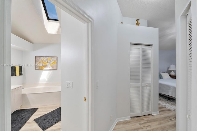 hall featuring a skylight, light wood-type flooring, and a textured ceiling