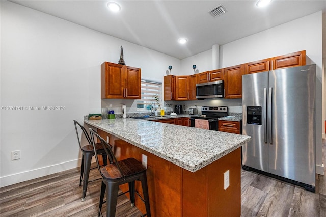 kitchen with kitchen peninsula, a kitchen bar, appliances with stainless steel finishes, and hardwood / wood-style flooring