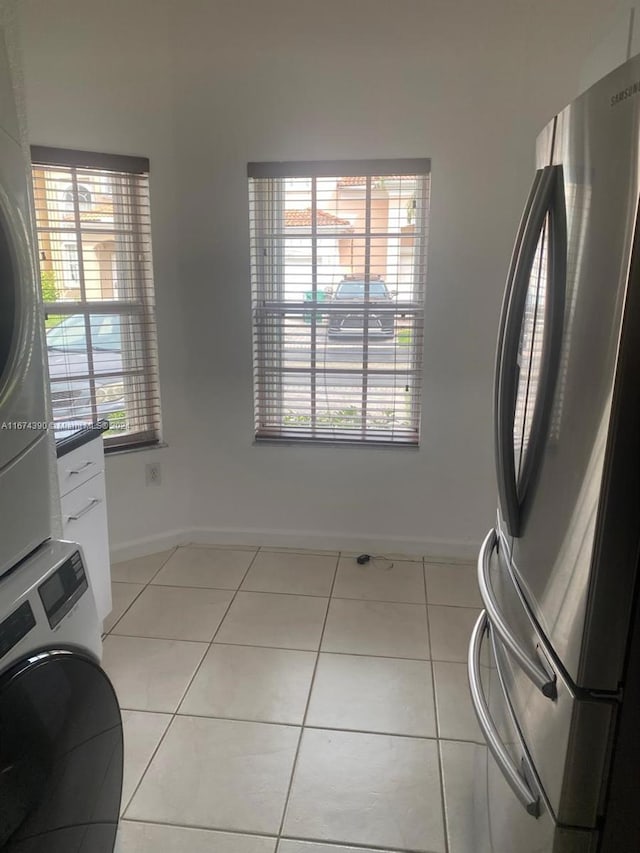 laundry area featuring a wealth of natural light, stacked washing maching and dryer, and light tile patterned floors