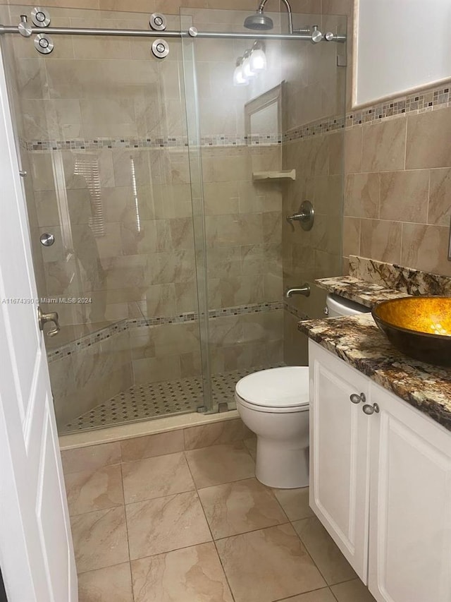 bathroom featuring toilet, tile walls, vanity, and a shower with shower door