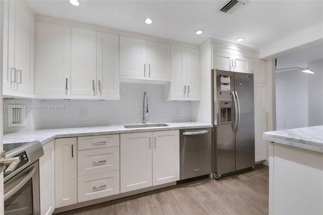 kitchen with decorative backsplash, white cabinetry, light wood-type flooring, sink, and stainless steel appliances