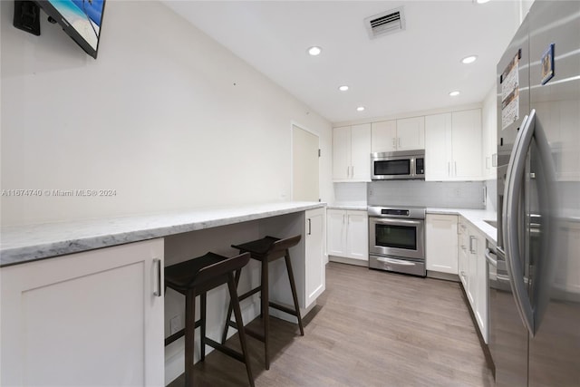 kitchen with light stone countertops, light wood-type flooring, white cabinetry, appliances with stainless steel finishes, and tasteful backsplash