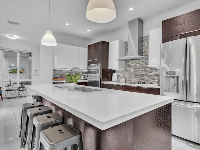 kitchen with dark brown cabinetry, wall chimney exhaust hood, a kitchen breakfast bar, decorative light fixtures, and appliances with stainless steel finishes