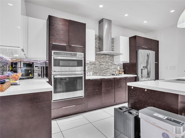 kitchen with white cabinets, wall chimney exhaust hood, appliances with stainless steel finishes, tasteful backsplash, and light tile patterned flooring