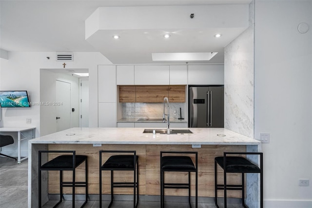 kitchen with a kitchen breakfast bar, sink, high end refrigerator, and white cabinets