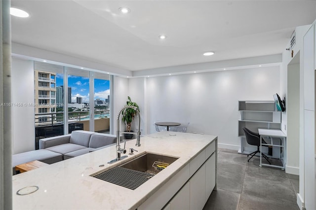 kitchen with light stone countertops, white cabinets, sink, and concrete flooring