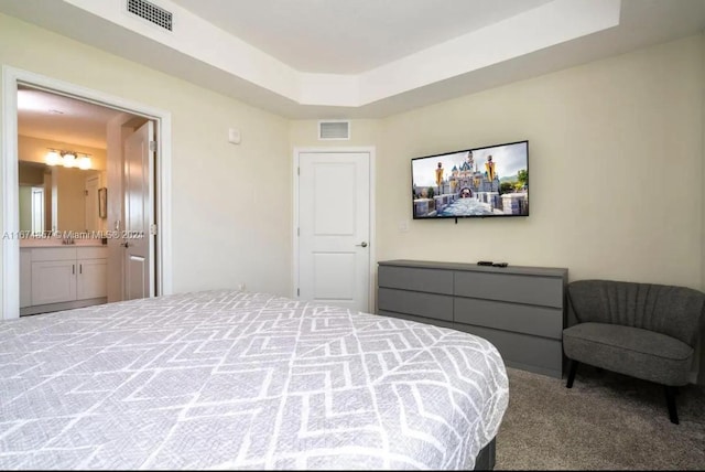 carpeted bedroom featuring a tray ceiling and ensuite bath