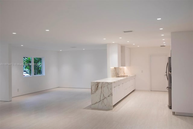 interior space featuring backsplash, black electric stovetop, stainless steel fridge, light stone countertops, and white cabinetry