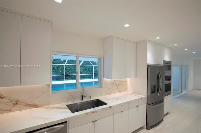 kitchen featuring sink, decorative backsplash, appliances with stainless steel finishes, light stone counters, and white cabinetry