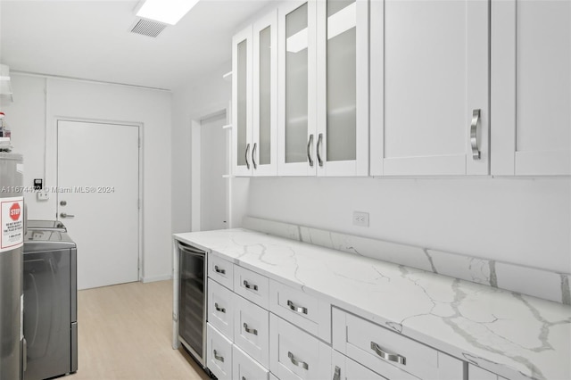 kitchen featuring white cabinets, washer / dryer, wine cooler, and light stone countertops