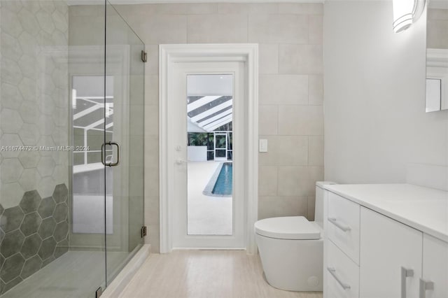 bathroom with vanity, a shower with door, hardwood / wood-style flooring, tile walls, and toilet