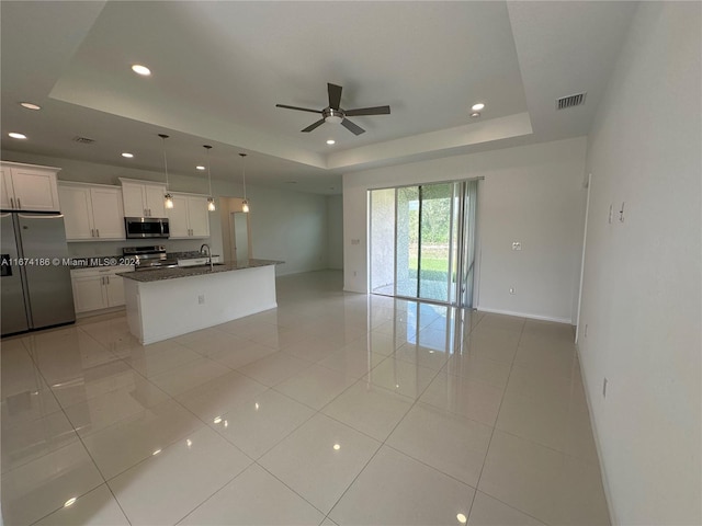 kitchen featuring an island with sink, white cabinetry, stainless steel appliances, and a raised ceiling