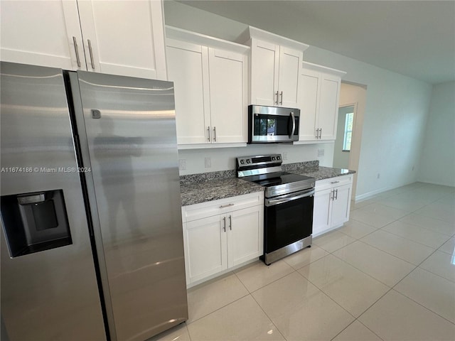 kitchen featuring appliances with stainless steel finishes, light tile patterned flooring, white cabinets, and dark stone countertops