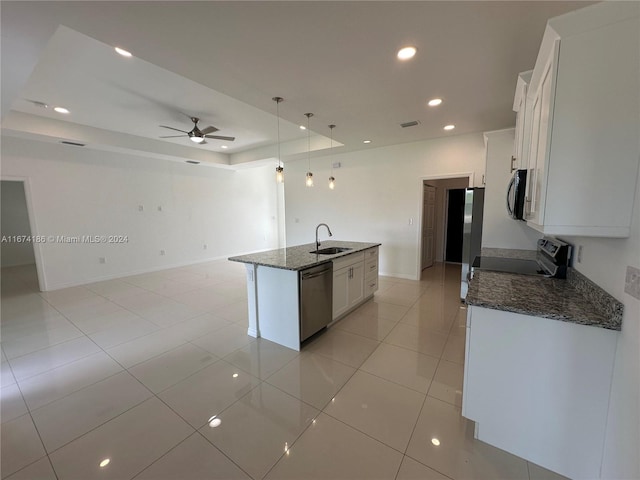 kitchen featuring an island with sink, stainless steel appliances, dark stone countertops, sink, and white cabinets