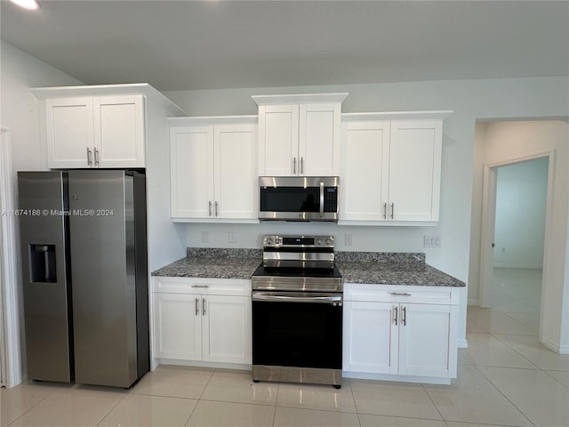 kitchen featuring light tile patterned floors, appliances with stainless steel finishes, dark stone counters, and white cabinets