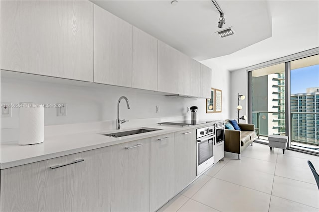 kitchen with rail lighting, stainless steel oven, sink, black stovetop, and light tile patterned floors