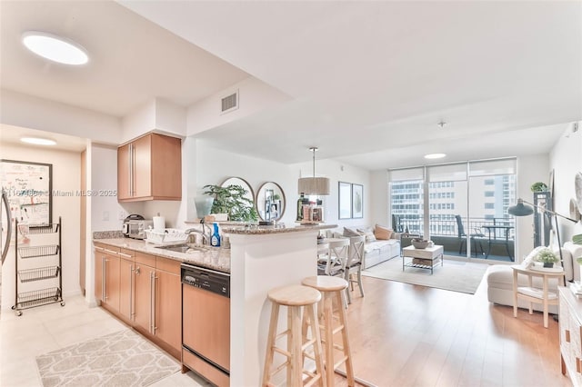 kitchen featuring kitchen peninsula, a kitchen breakfast bar, dishwashing machine, sink, and light stone countertops