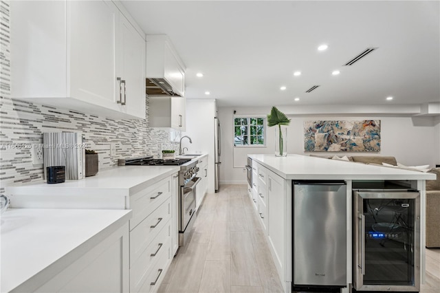 kitchen with tasteful backsplash, beverage cooler, appliances with stainless steel finishes, white cabinetry, and light hardwood / wood-style flooring