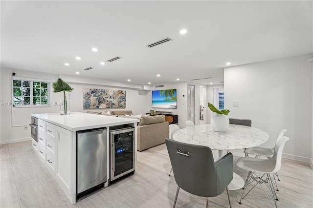 kitchen featuring white cabinets, beverage cooler, a kitchen island, light hardwood / wood-style flooring, and stainless steel appliances