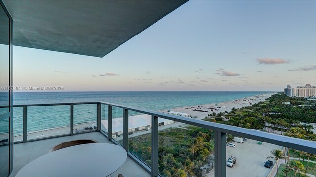 balcony at dusk featuring a view of the beach and a water view