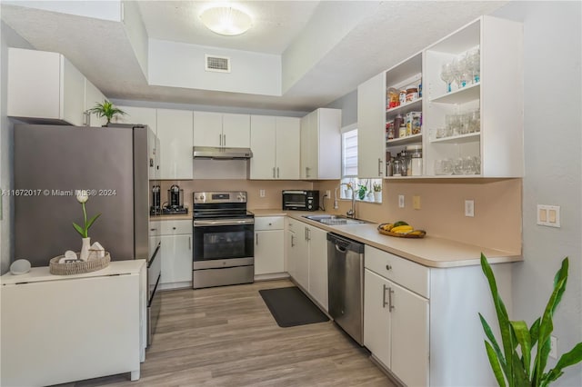 kitchen featuring stainless steel appliances, a raised ceiling, sink, light hardwood / wood-style flooring, and white cabinets