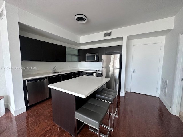 kitchen with a kitchen island, appliances with stainless steel finishes, sink, a kitchen breakfast bar, and dark wood-type flooring