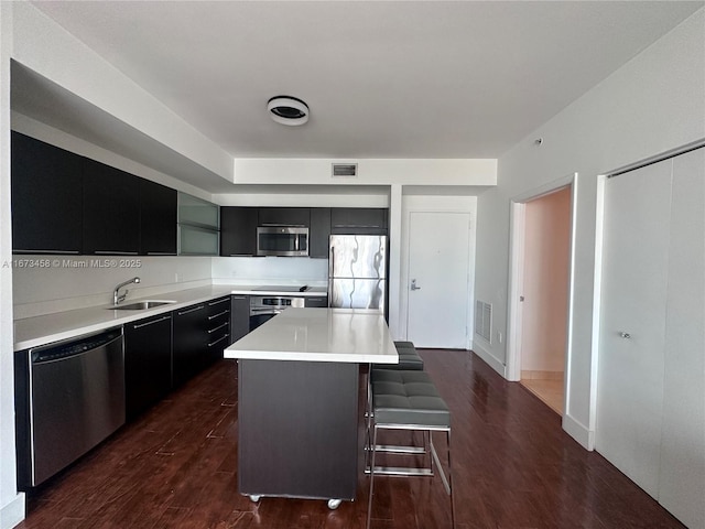 kitchen with a kitchen island, sink, a kitchen bar, stainless steel appliances, and dark wood-type flooring